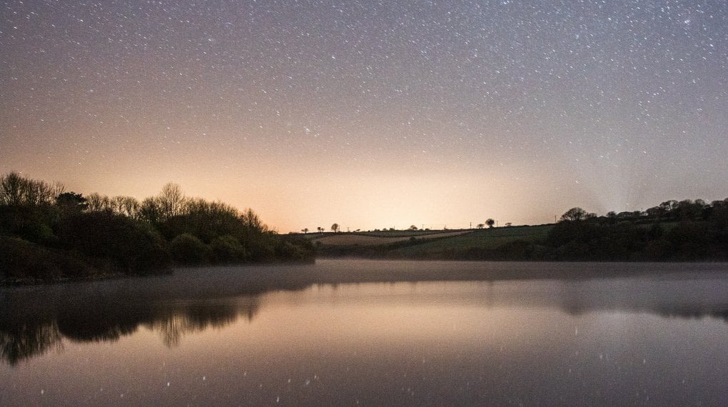 View over reservoir at night with stars reflecting on the water's surface